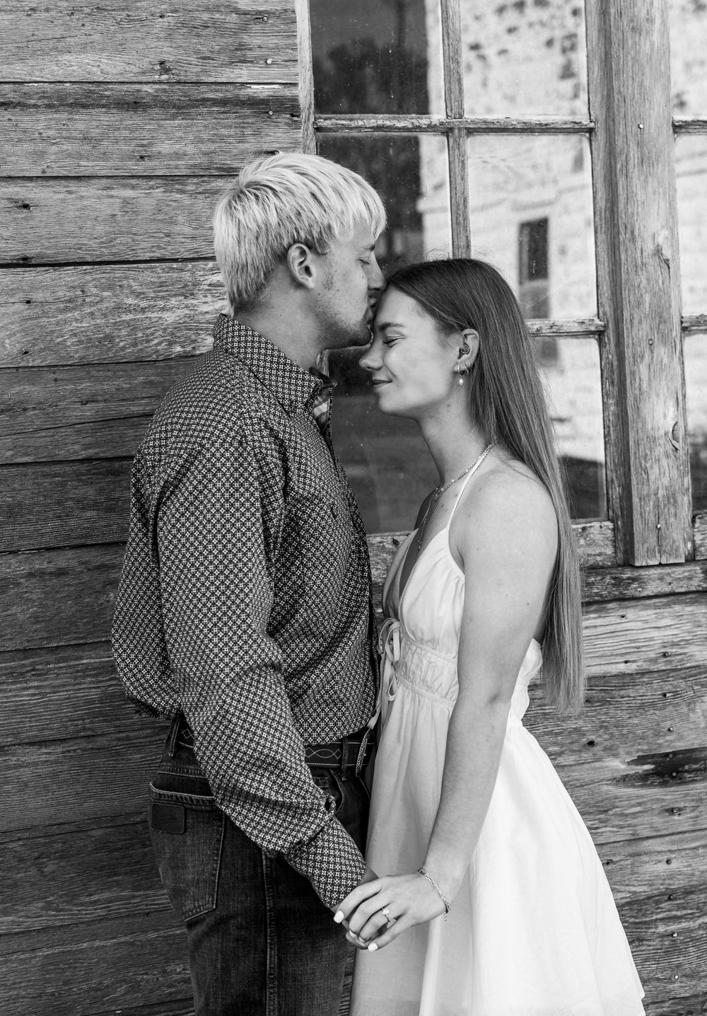 Black and white portrait of couple in tender moment against rustic wooden wall.