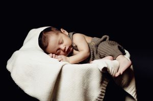 Sleeping newborn baby wrapped in cozy knit blanket on dark background.