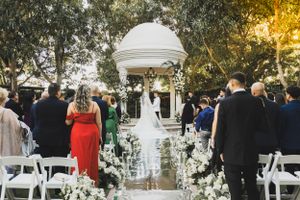 Beautiful outdoor wedding ceremony under a white gazebo with floral-lined aisle.