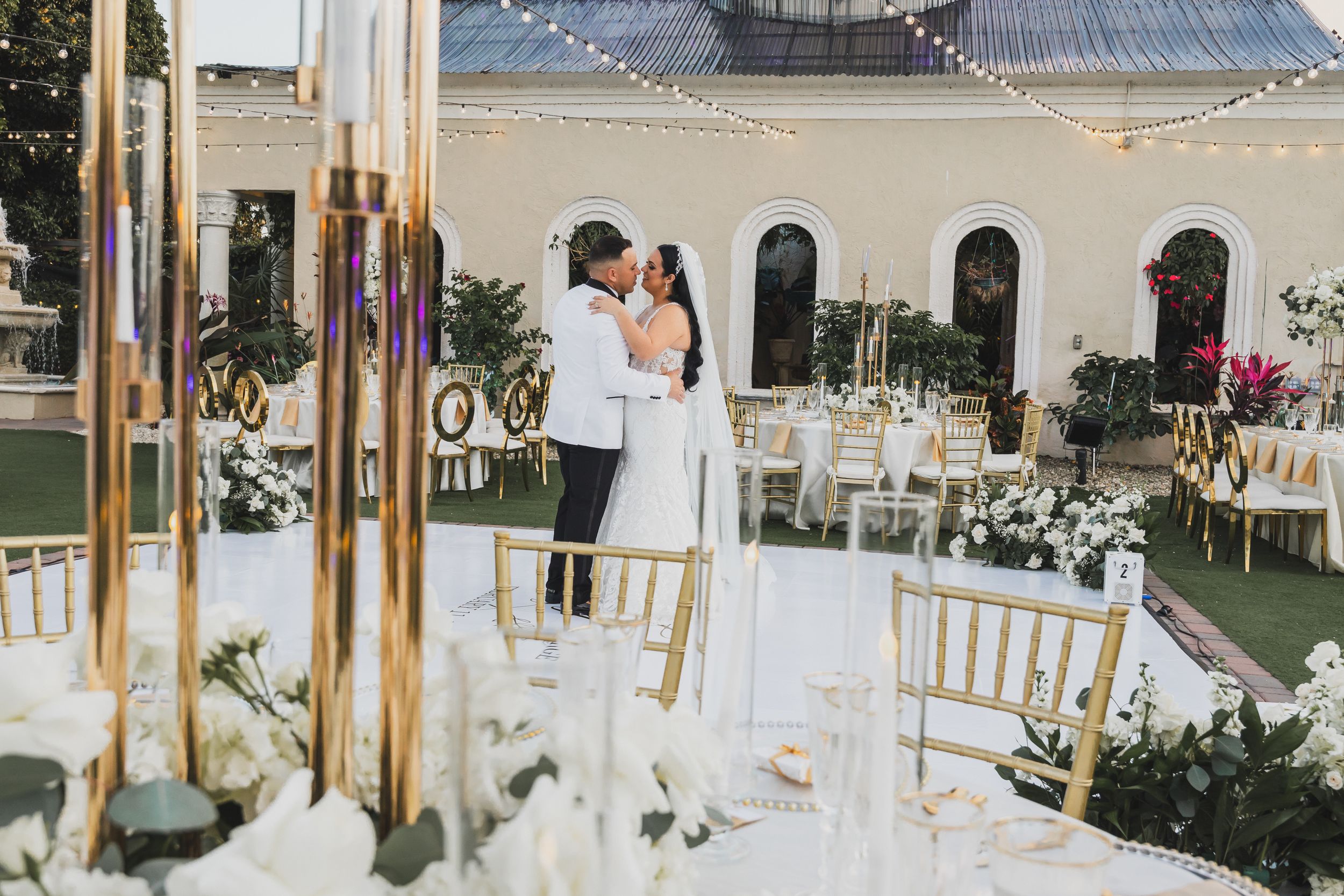 Elegant outdoor wedding reception setup with gold pillars and white decor at sunset.