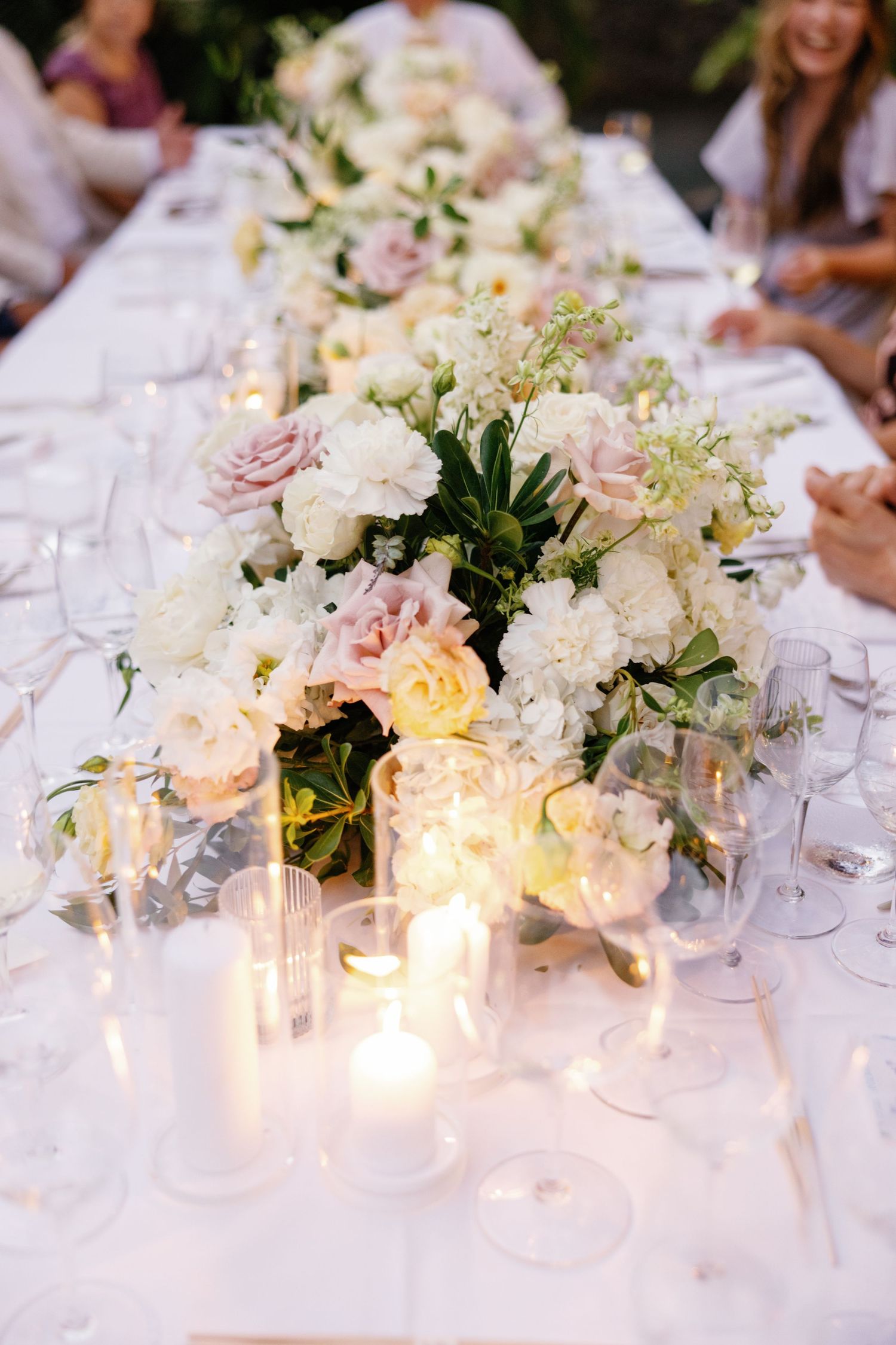 Romantic wedding reception table with white and blush floral centerpiece and glowing candles.