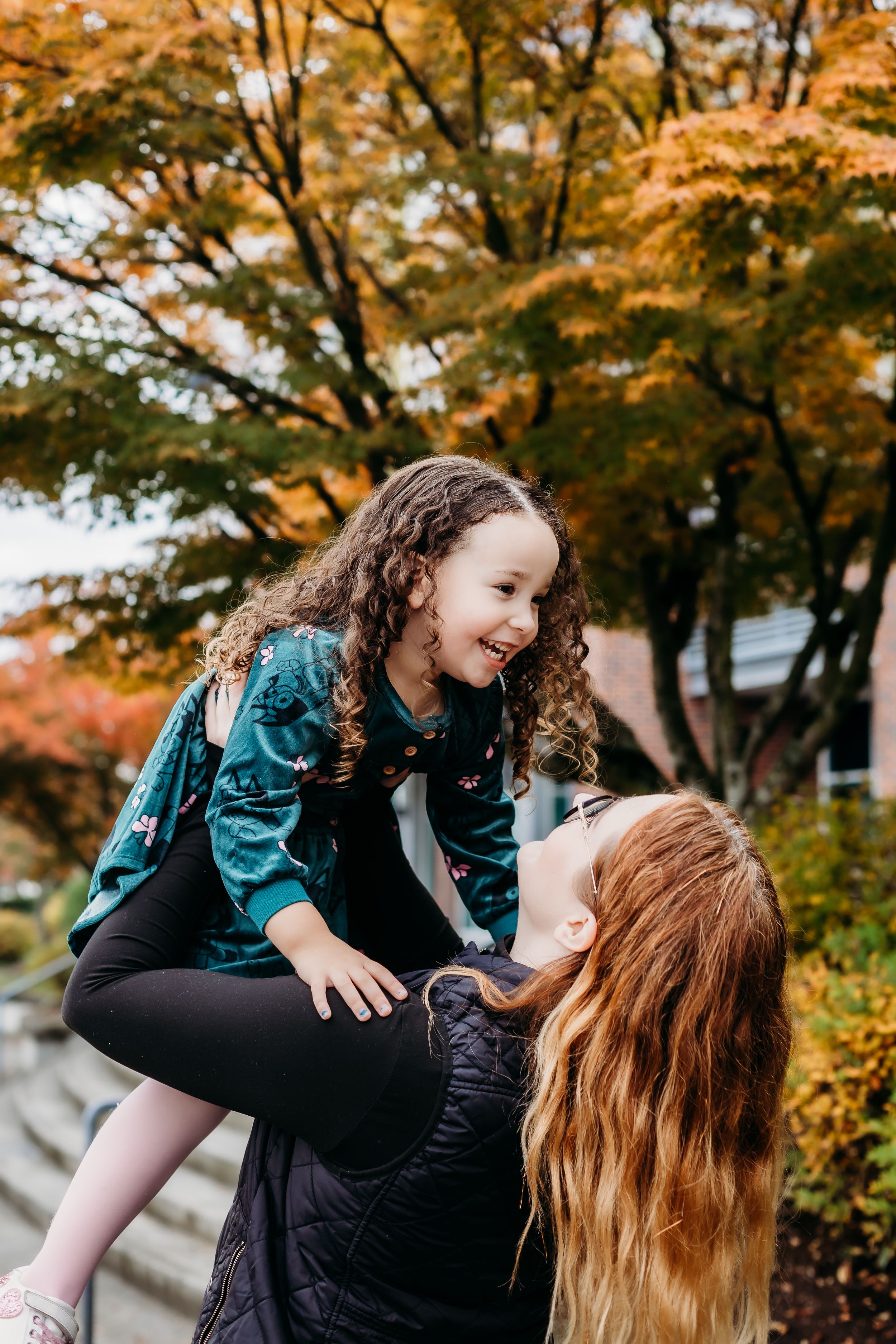 Autumn outdoor scene of playful moment between parent and child among colorful fall foliage.