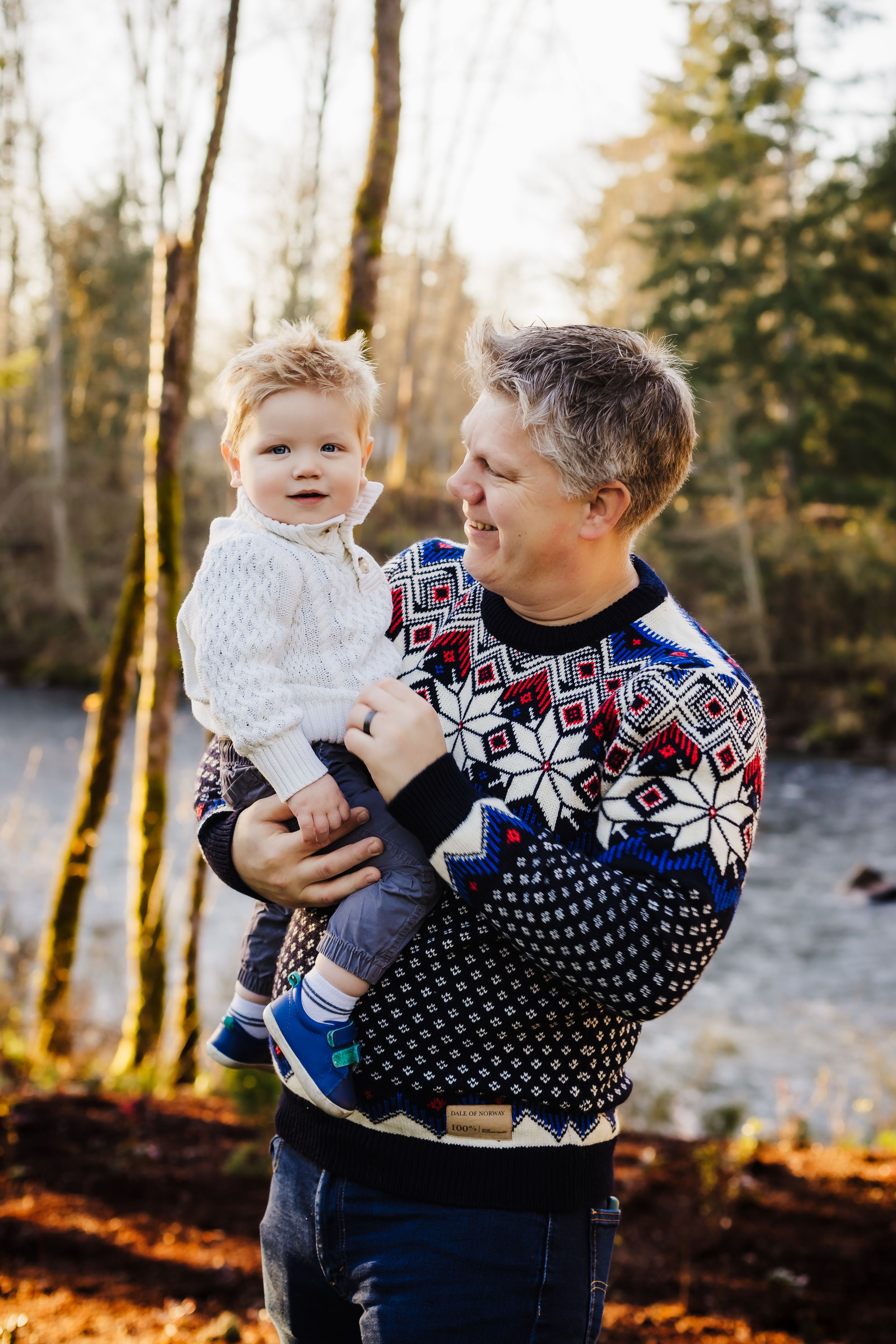 Winter portrait of adult and child wearing matching holiday sweaters in snowy forest setting.