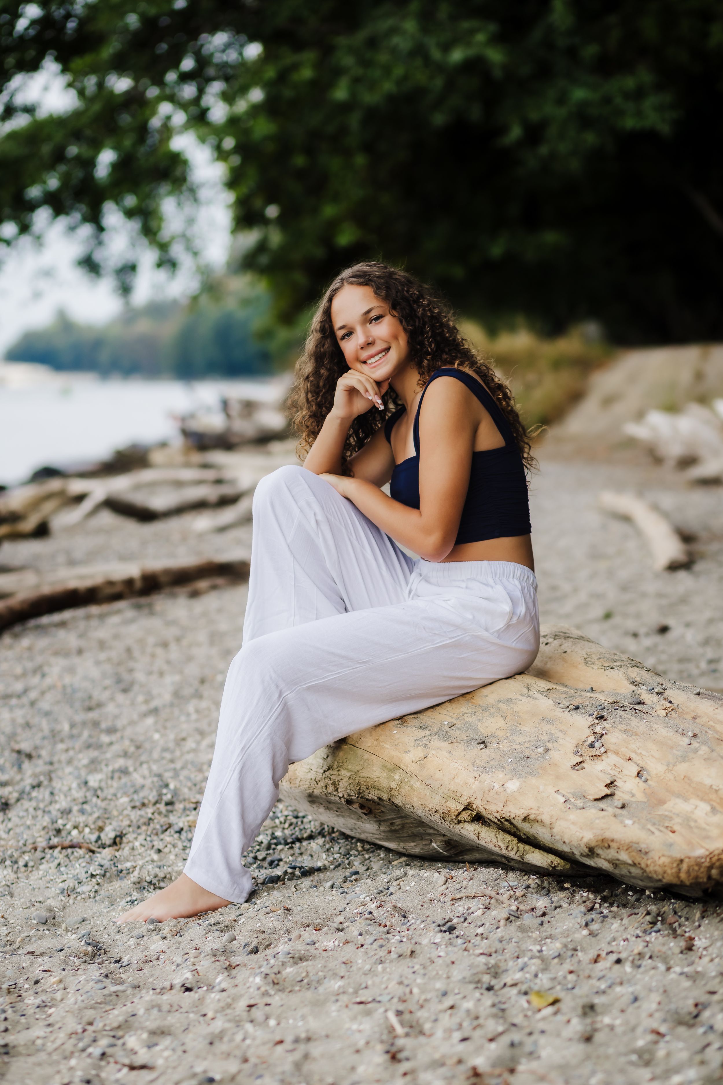 Person in black top and white pants relaxes on rocky beach shore.