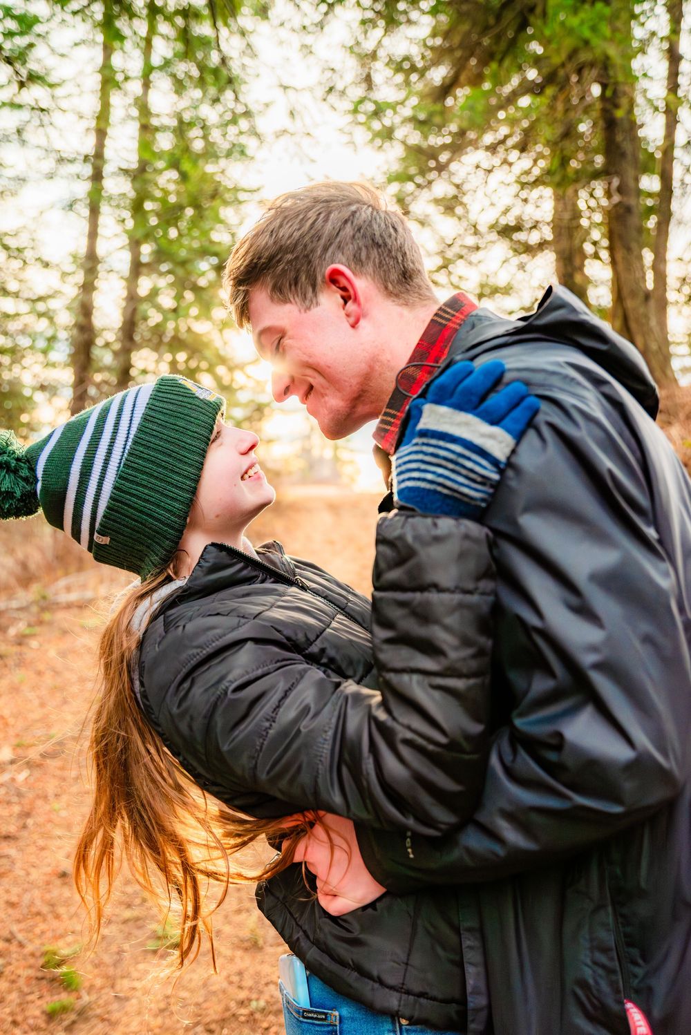 A couple shares a romantic moment in the woods during autumn while wearing winter coats and beanies.