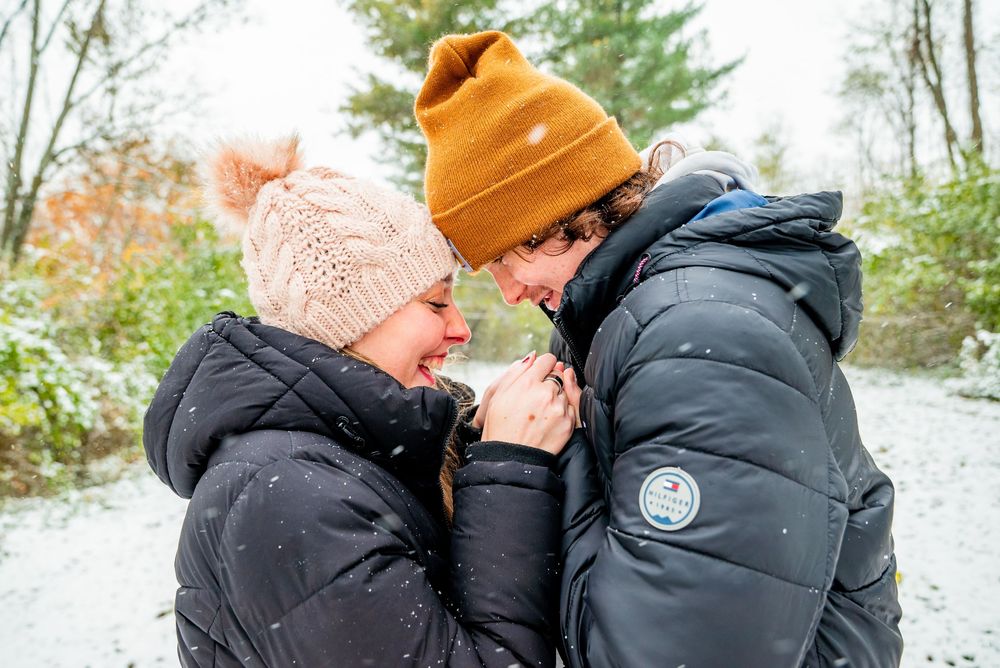 Two people in winter coats share an intimate moment outdoors in the snow.