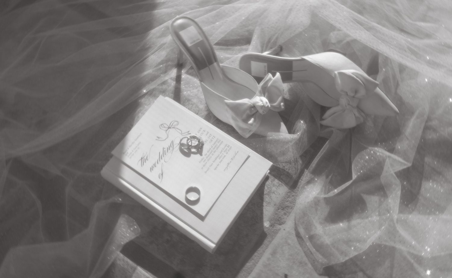 A black and white image of wedding rings displayed on an elegant box with flowing fabric.