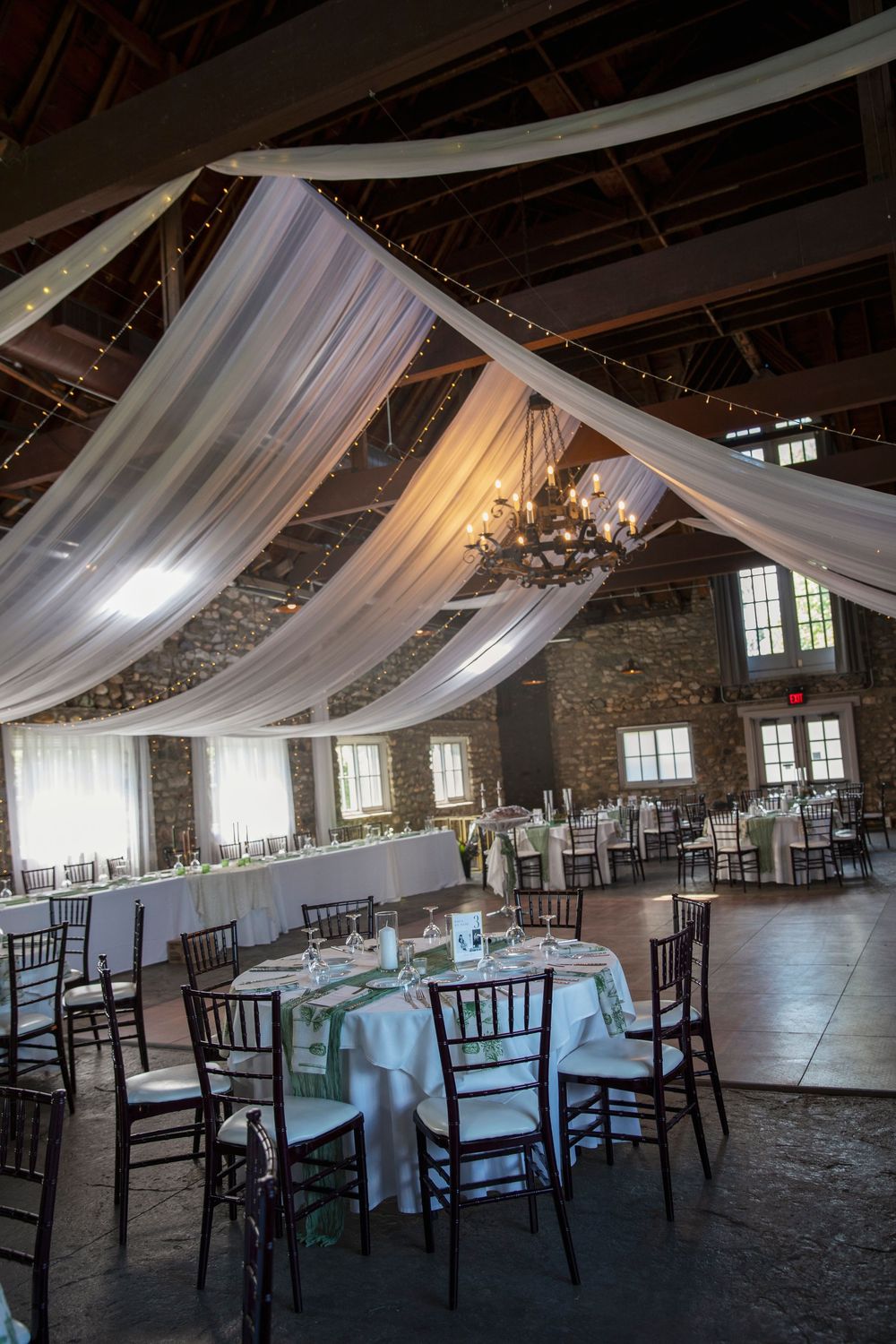 An elegant wedding reception venue with draped white fabric and chandeliers in a rustic stone building.