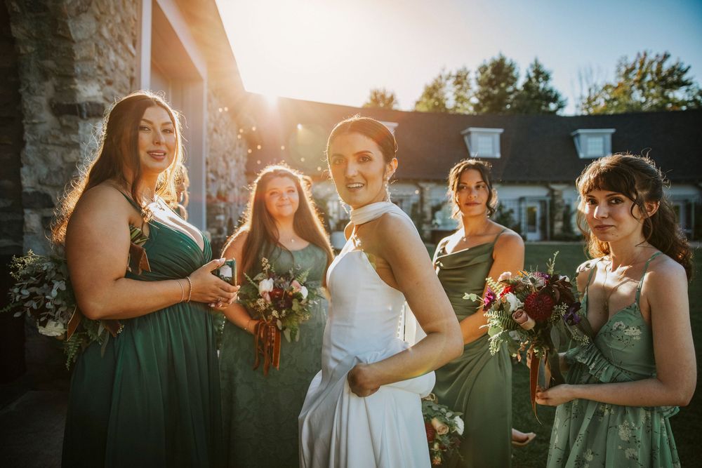 A wedding party poses together at sunset outside a stone building.