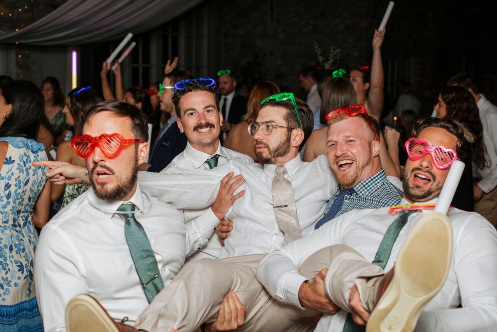 Wedding guests wearing colorful sunglasses pose playfully during reception celebrations.