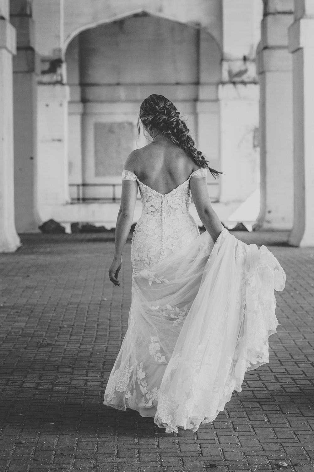Black and white photo of flowing wedding dress train on brick paved floor.