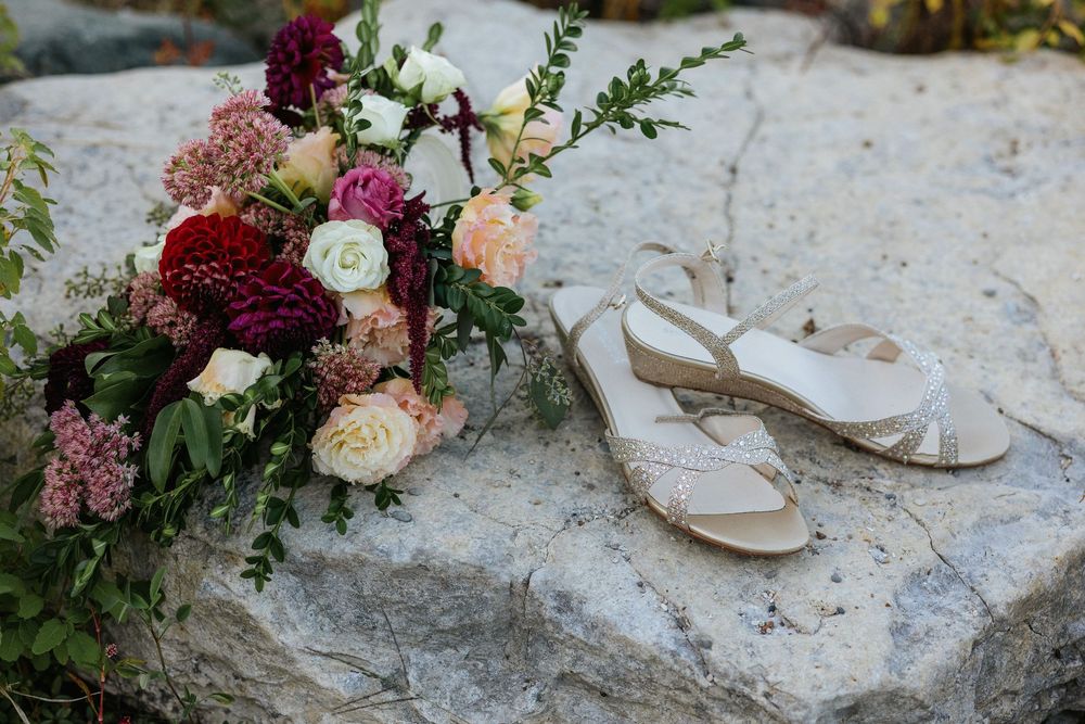 Wedding bouquet with burgundy and cream flowers arranged on natural stone surface.