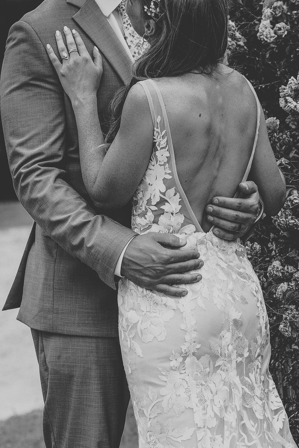 An intimate black and white photo showing the back details of a lace wedding dress during an embrace.