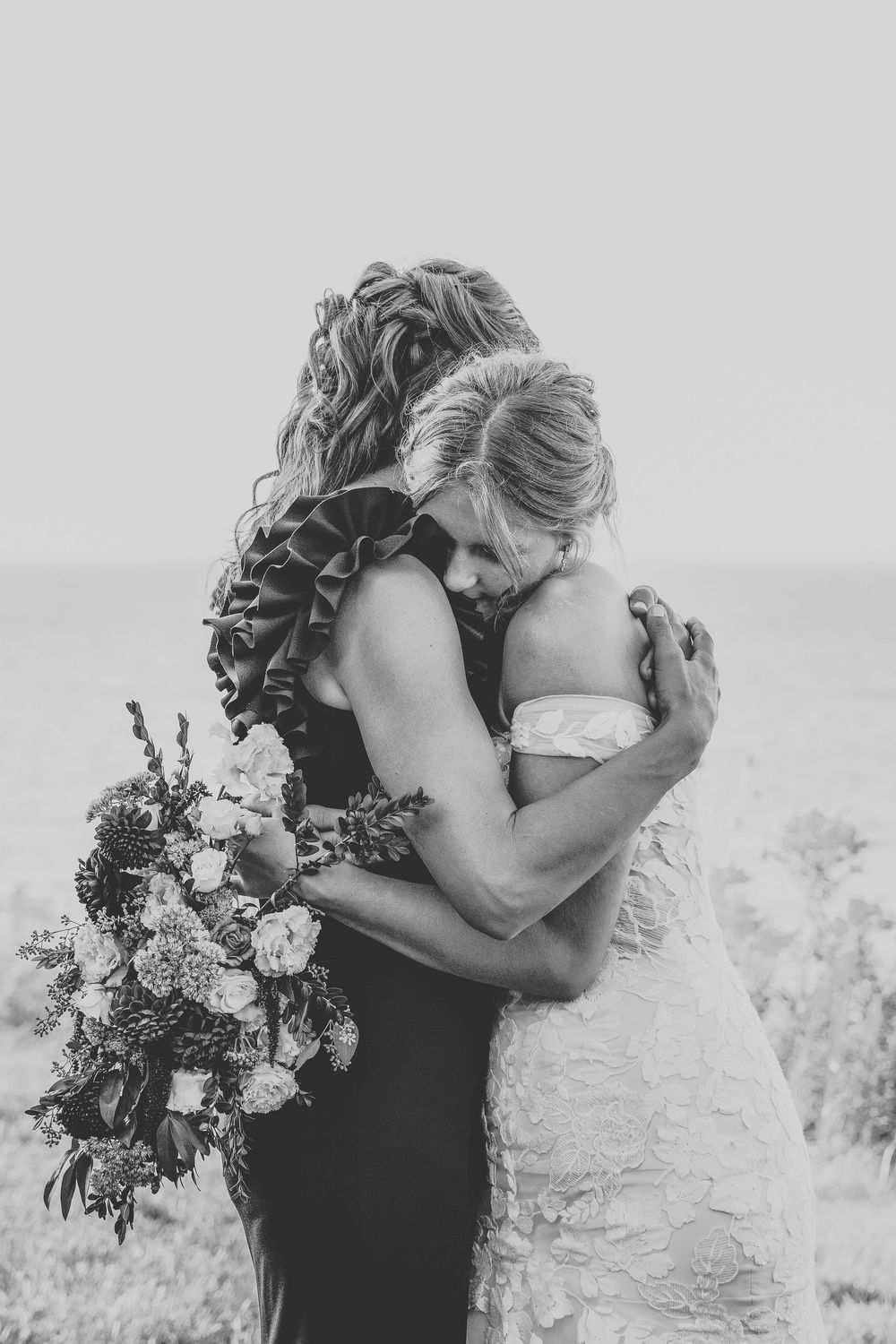 Intimate wedding moment captured in soft black and white tones with floral bouquet.