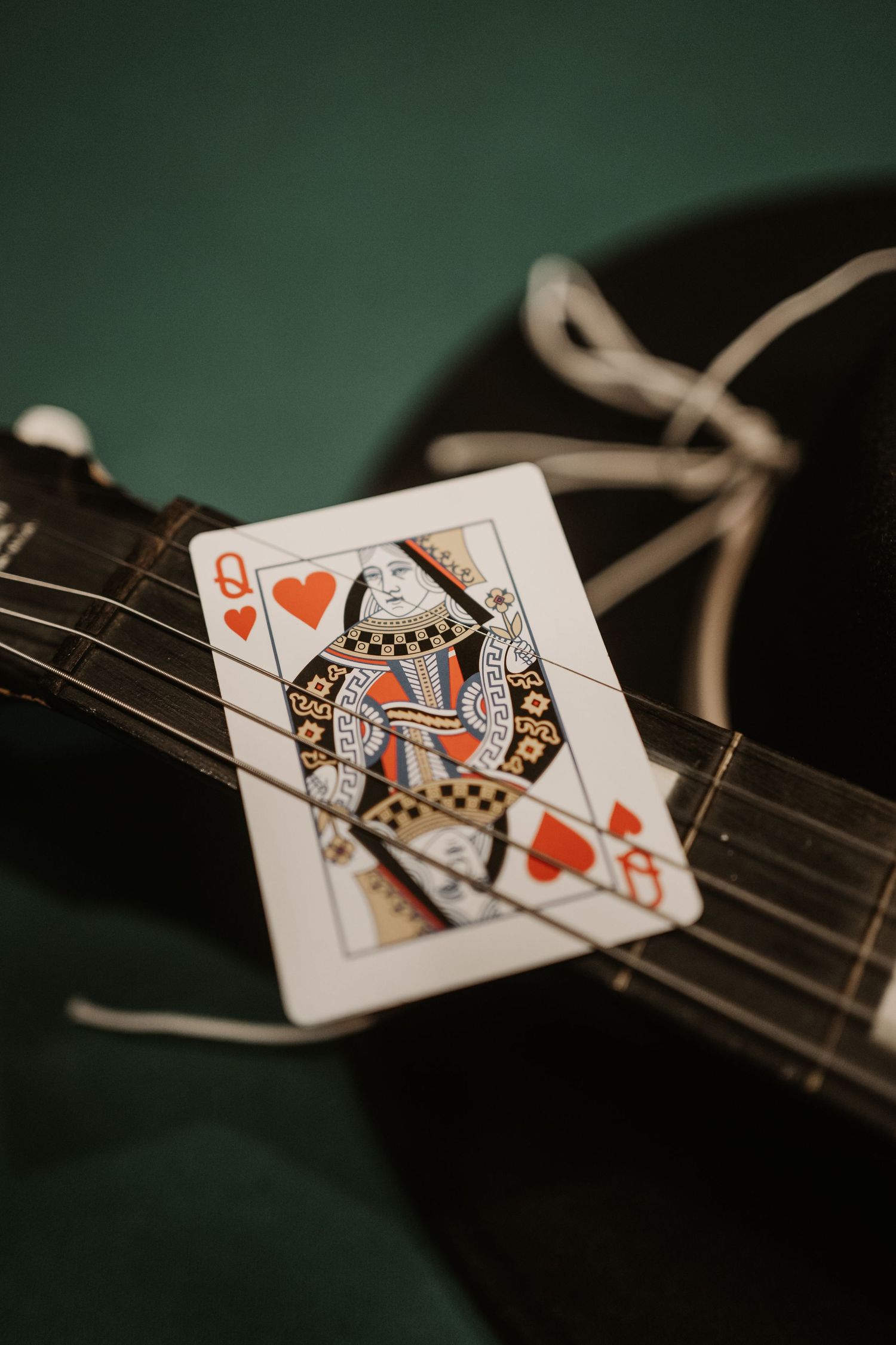 Queen of Hearts playing card resting on guitar strings with dark background.