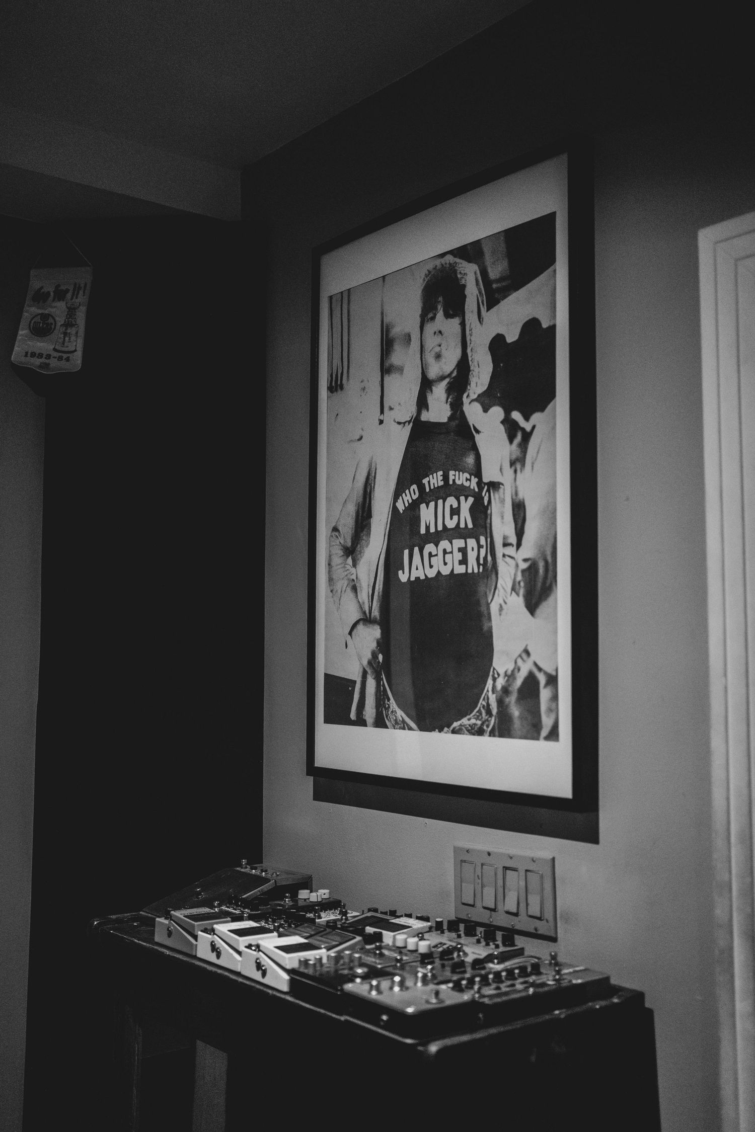 Black and white photo of DJ equipment below a framed Mick Jagger poster in a dimly lit room.