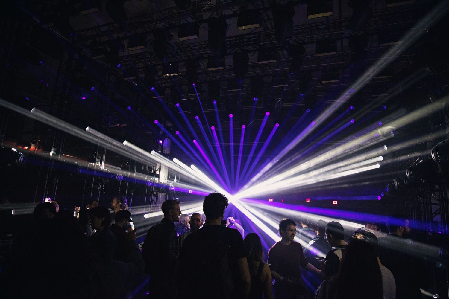 Vibrant laser light show illuminates a dark nightclub with blue and white beams above a crowd.