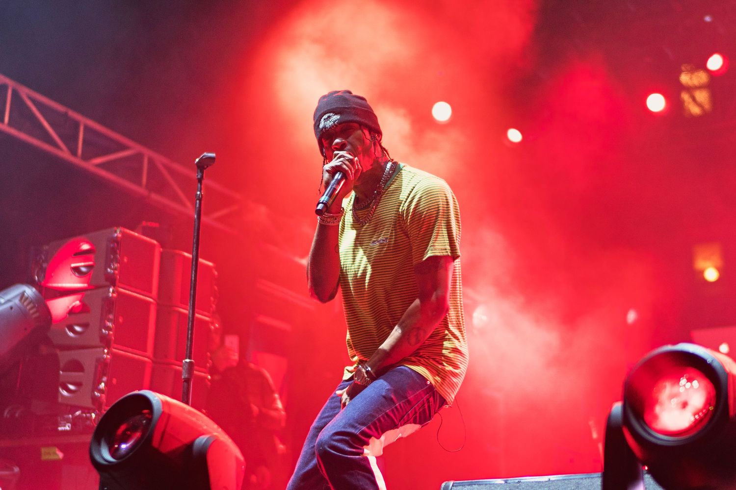 Male rapper performing on stage under dramatic red lighting with stage fog and concert lights.