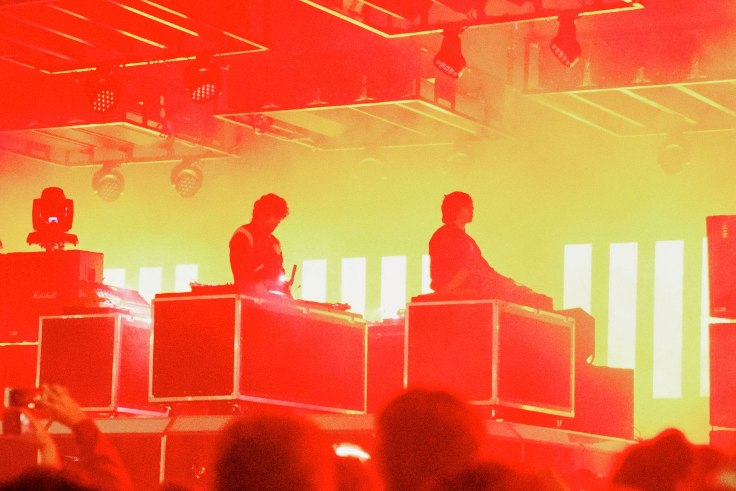 Two DJs performing on stage bathed in red and yellow lights at a live concert event.