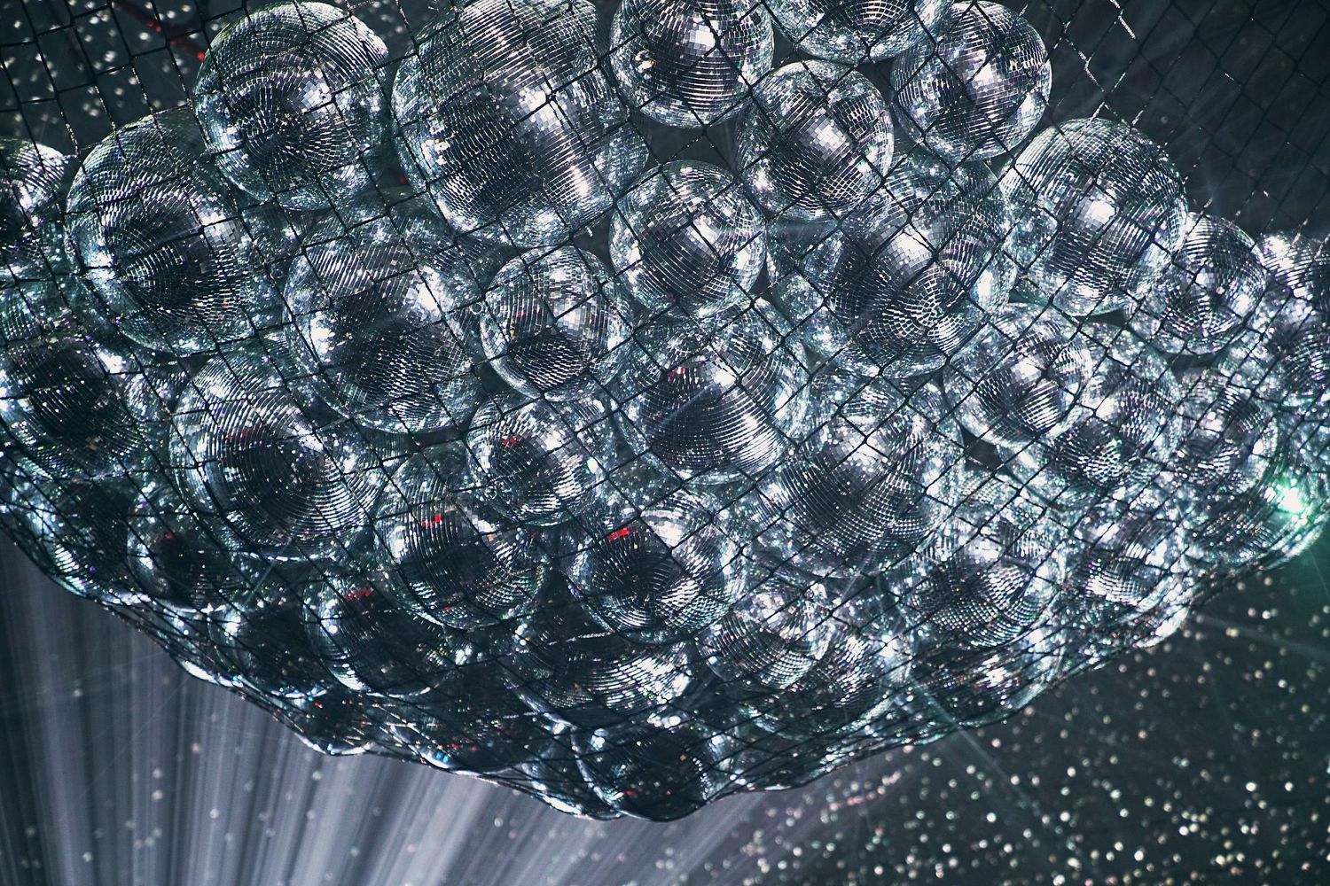 A stunning chandelier made of clustered reflective silver disco balls illuminated by bright sparkling lights from below.