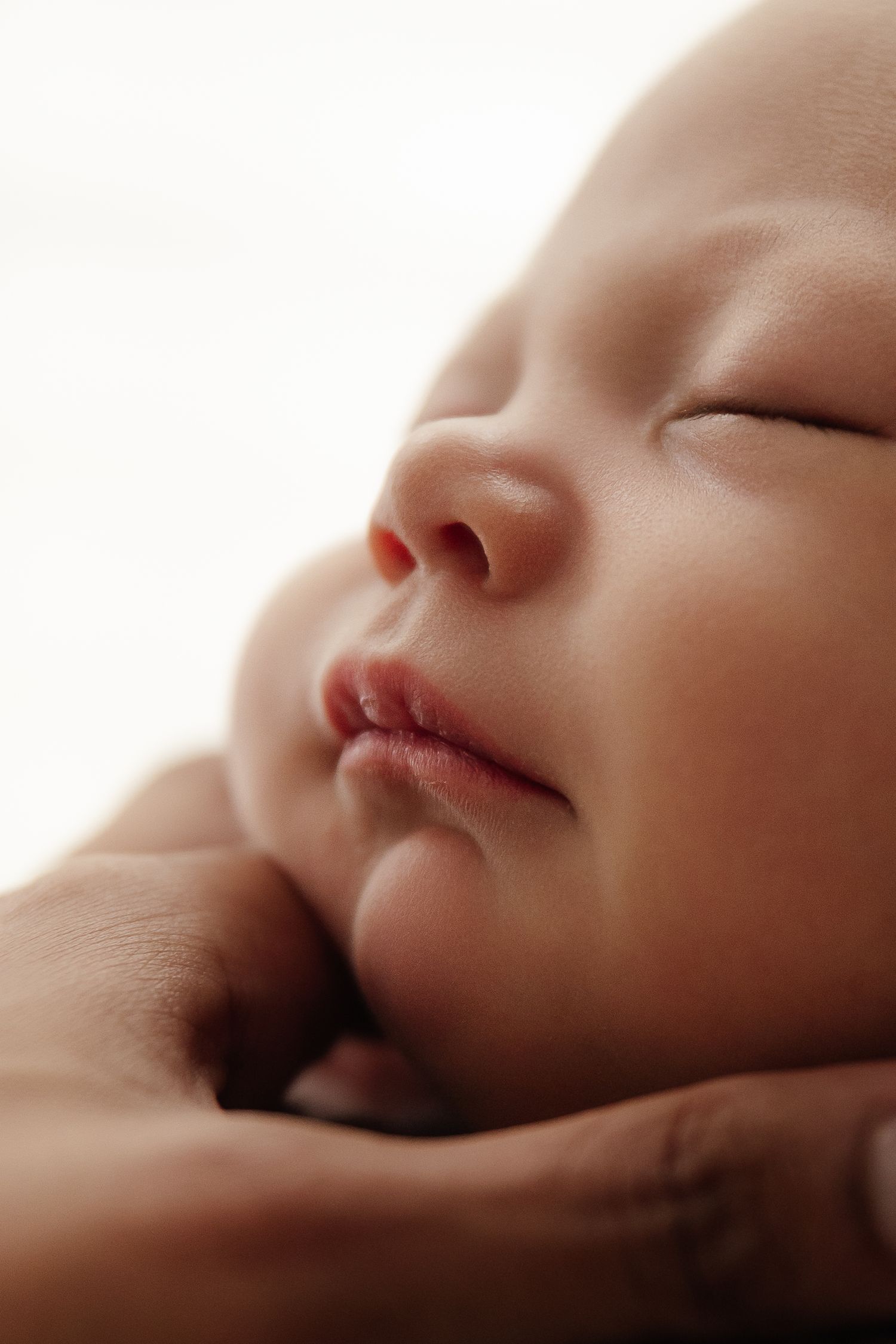 Newborn baby in white knit outfit sleeping peacefully.