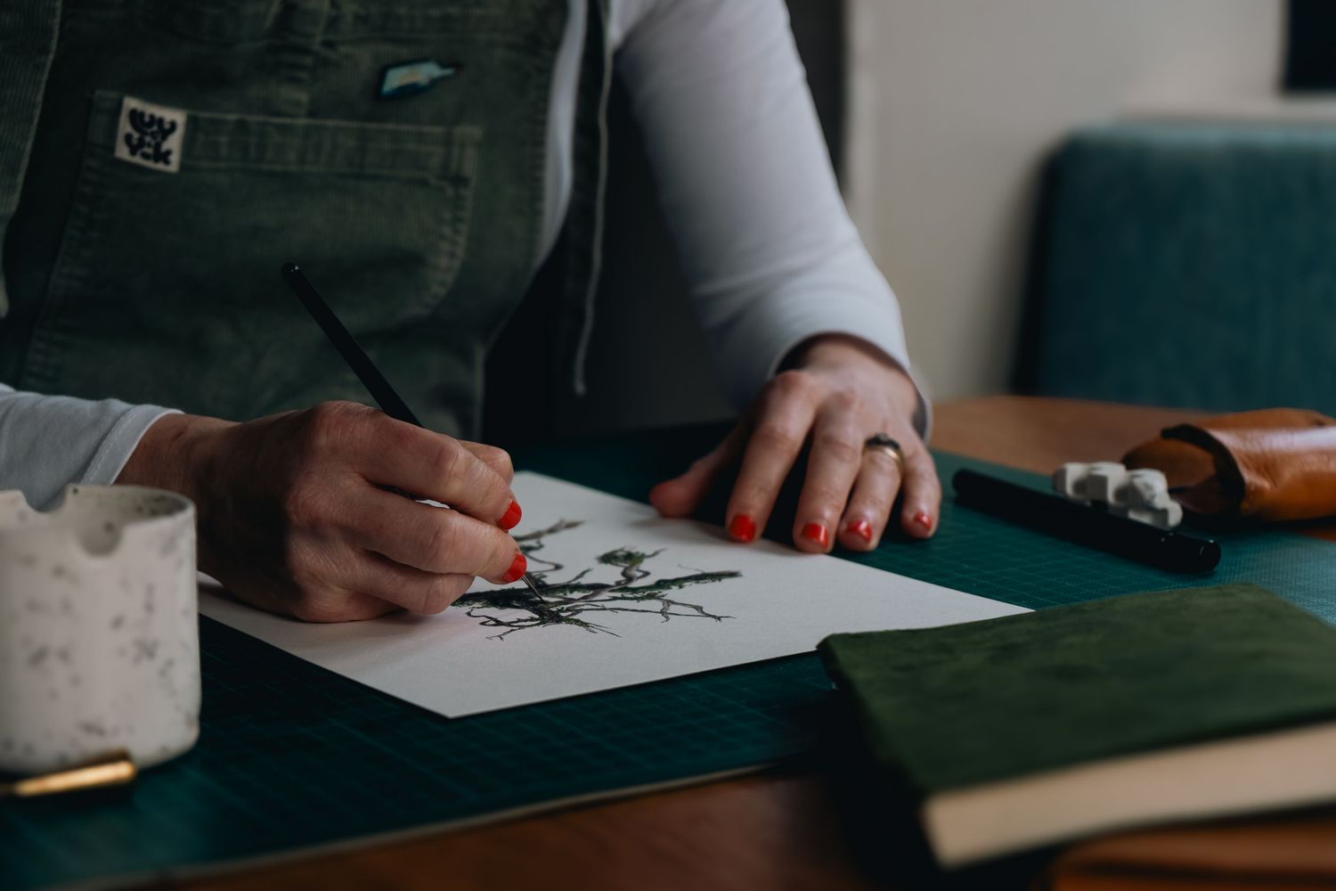 Close up photograph from a brand storytelling session of an illustrator in green painting at her kitchen table with paints and water pot