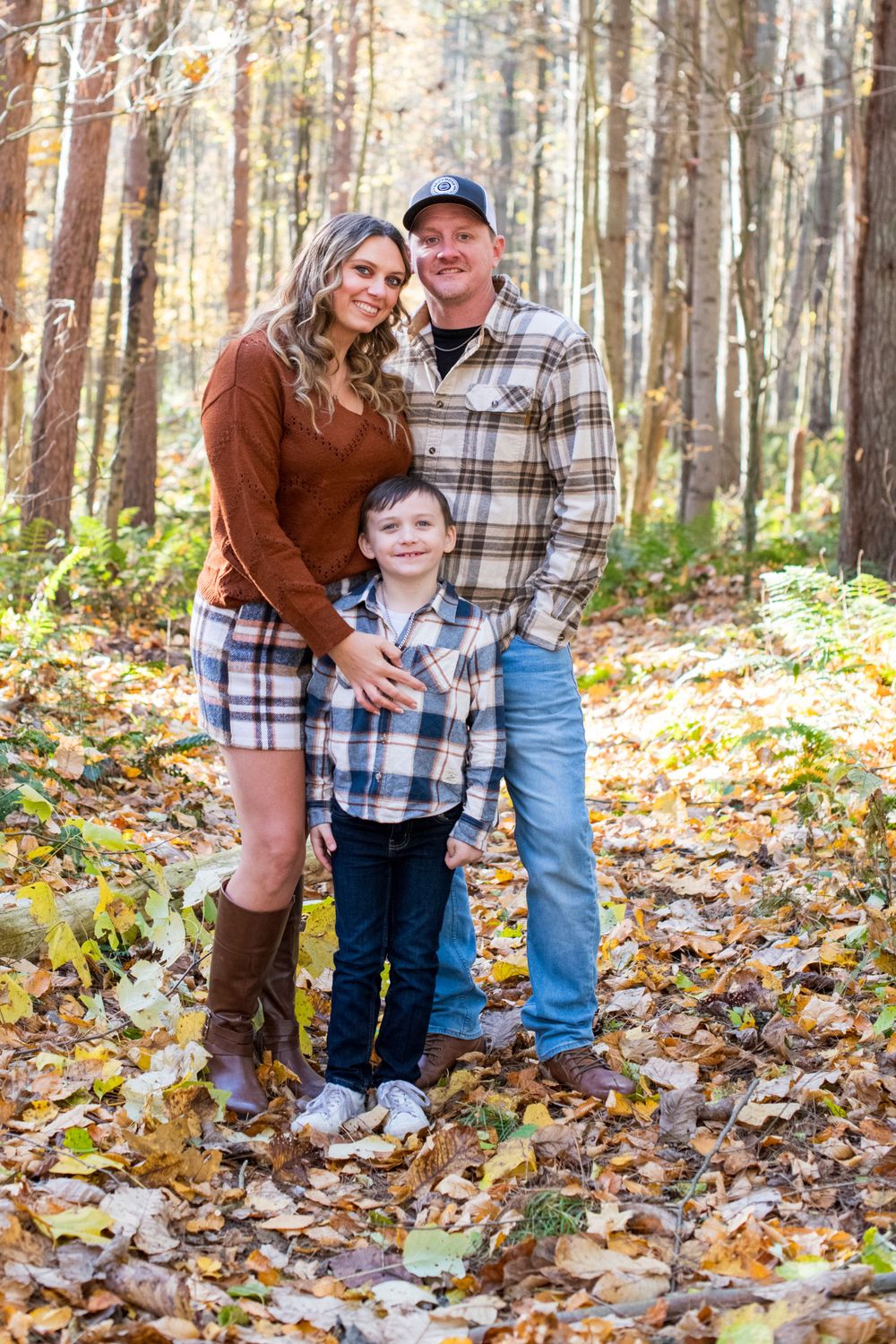 Family of three posing in autumn forest with colorful fall foliage, mother in rust sweater and boots.