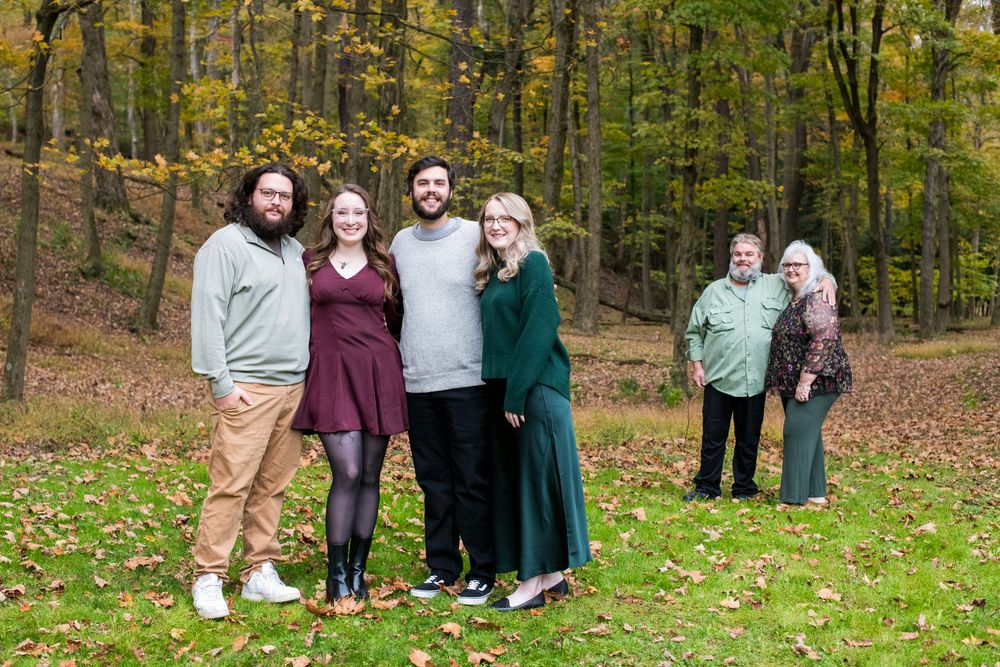 Family group of five posing outdoors in autumn forest setting with colorful fall foliage backdrop.