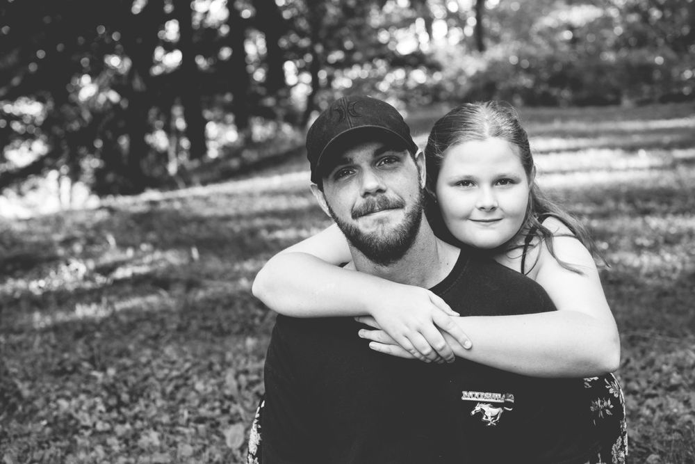 Black and white photo of a father and daughter hugging outdoors in a park.