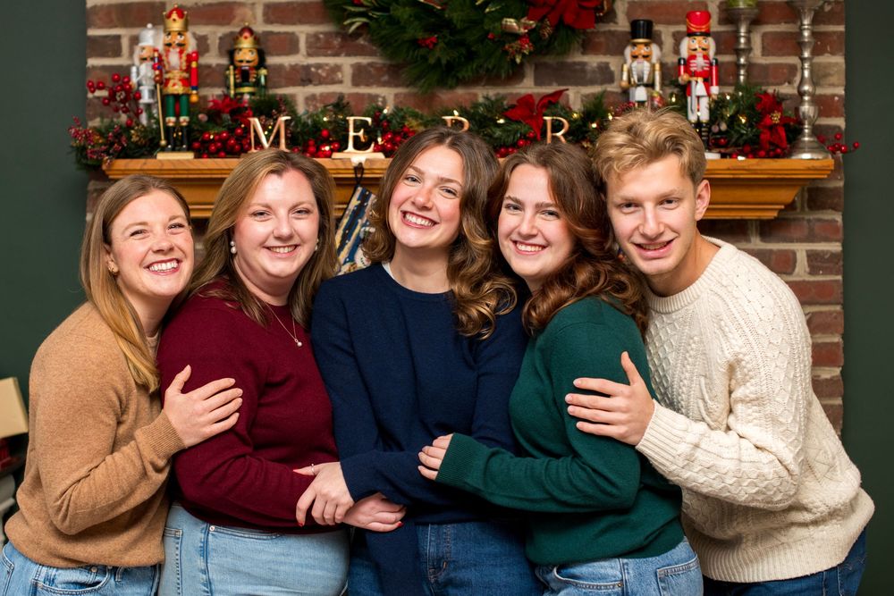 Five people smiling together in front of a festive Christmas fireplace mantel decorated with nutcrackers and garland.