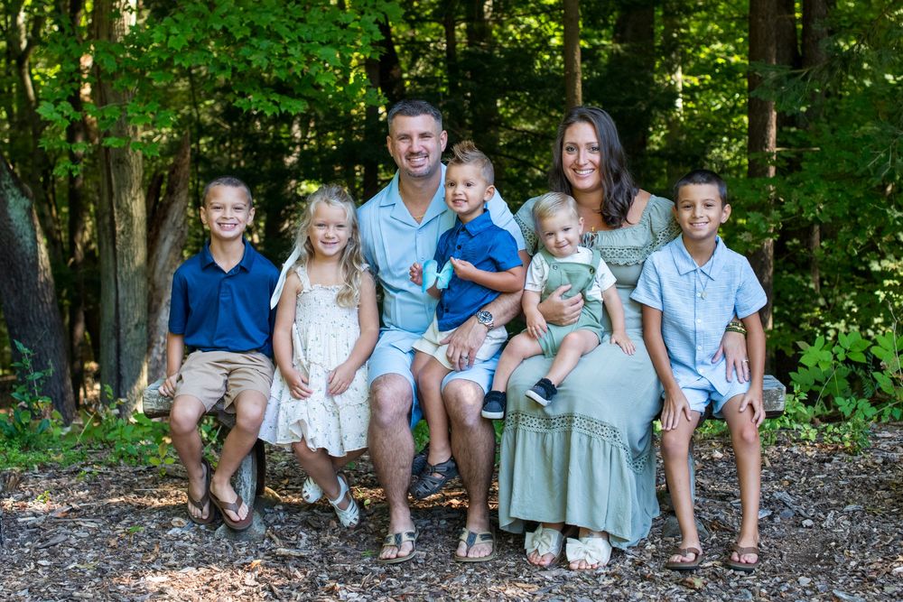 Happy family of seven posing outdoors in a lush green forest setting for a professional portrait photo.