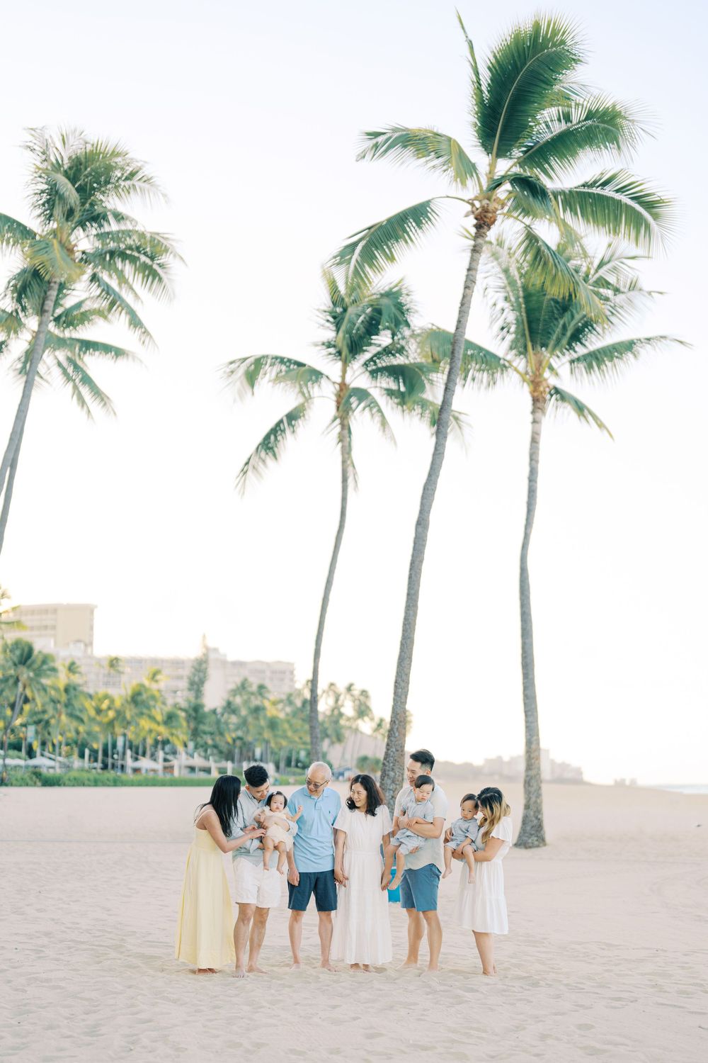 Family gathering under tall palm trees on a sandy beach during golden hour.
