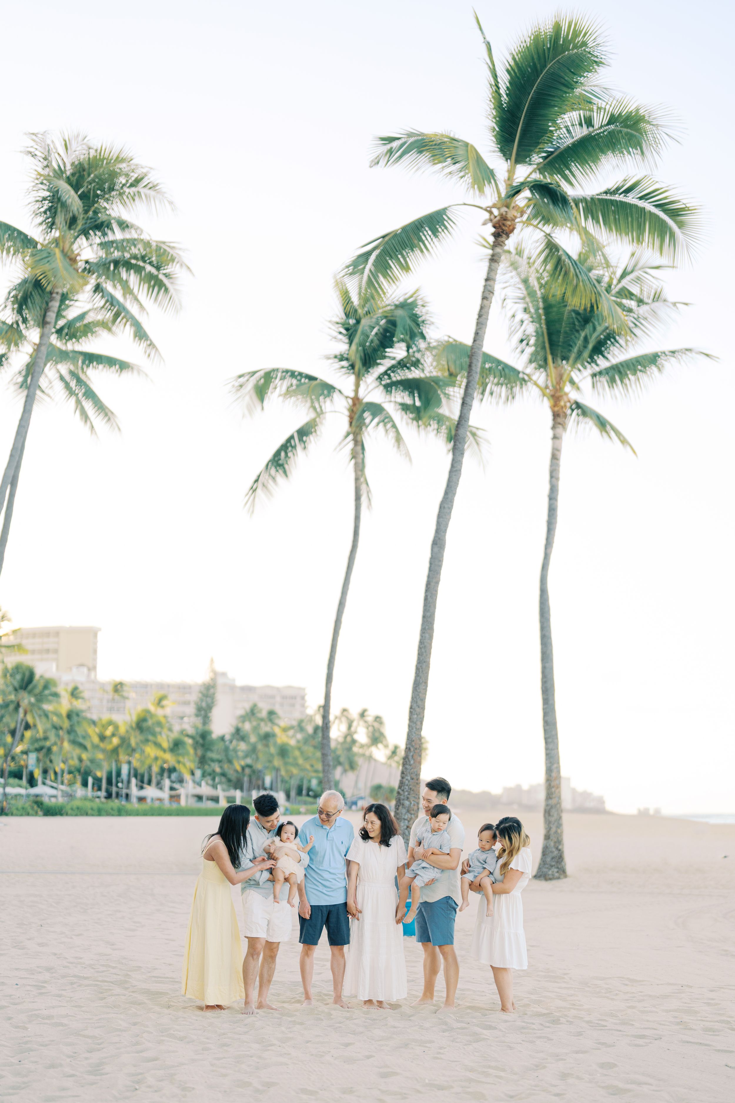 Family gathering under tall palm trees on a sandy beach during golden hour.