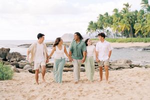 A family walks together along a scenic Hawaiian beach with palm trees and volcanic rocks in the background.