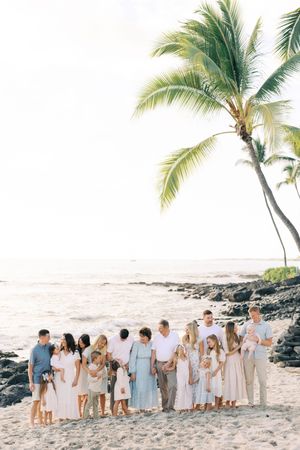 Large family group in coordinated white and blue outfits poses together on a Hawaiian beach at sunset.