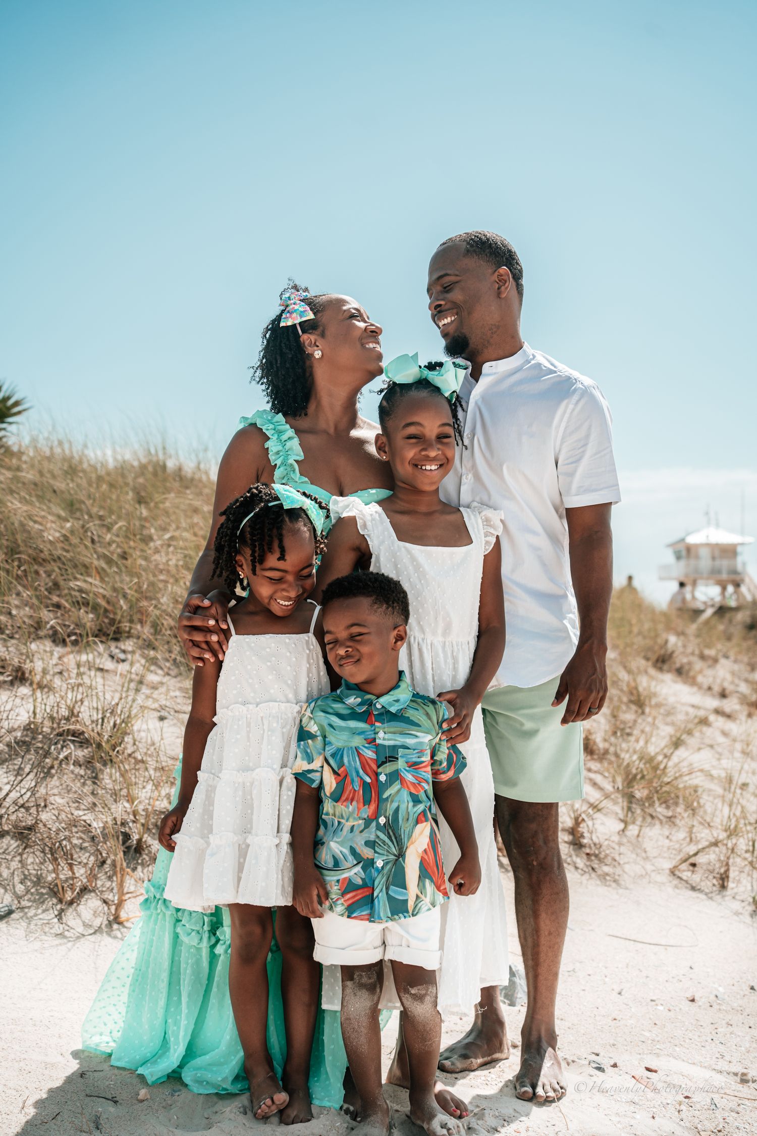 A family wearing coordinated white and mint green outfits poses together on a sandy beach dune.