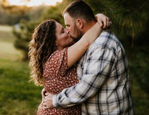 Couple sharing a romantic kiss outdoors at golden hour, woman in floral dress, man in plaid shirt.
