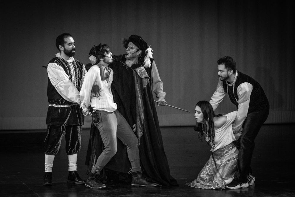 Black and white photo of five theater performers in period costumes during a dramatic stage production.