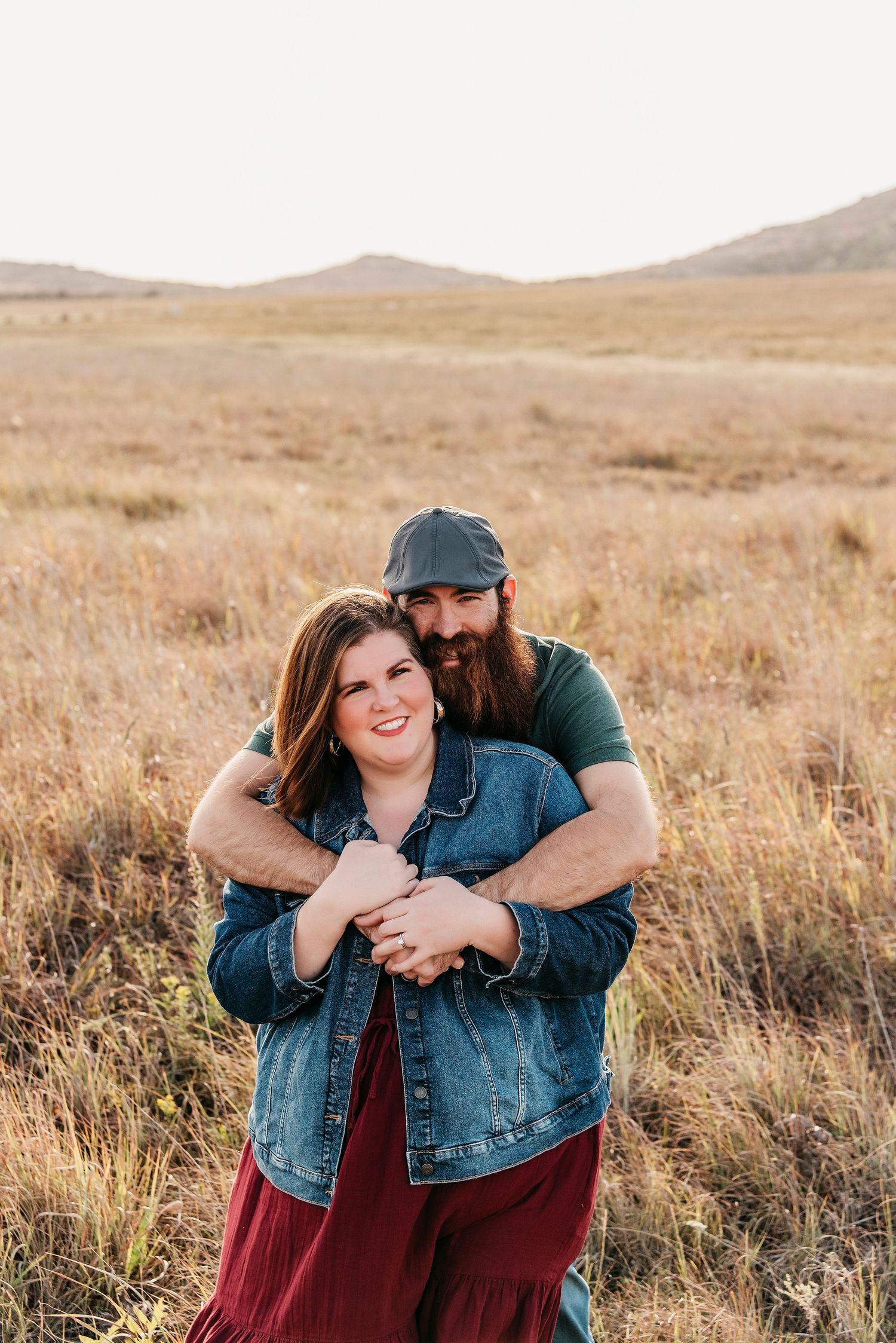 Couple embracing in casual attire during sunset photoshoot in open field.