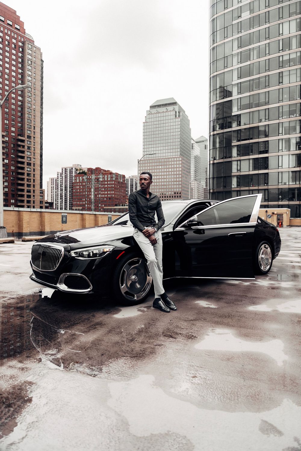A sleek black luxury car parked on a rooftop parking deck with modern high-rise buildings in the background.