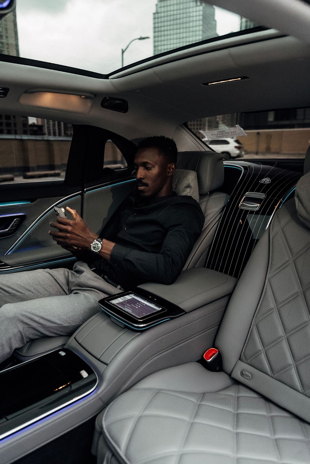 Luxurious car interior with quilted leather seats and ambient lighting shows passenger using smartphone in back seat.