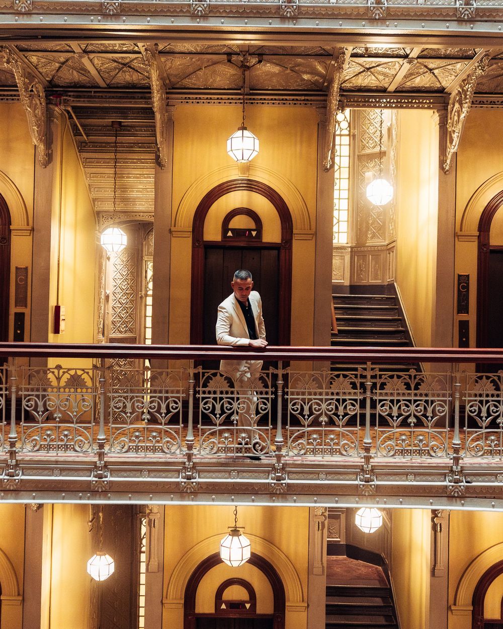 Ornate historic theater interior with multiple balcony levels featuring golden walls and vintage pendant lighting.