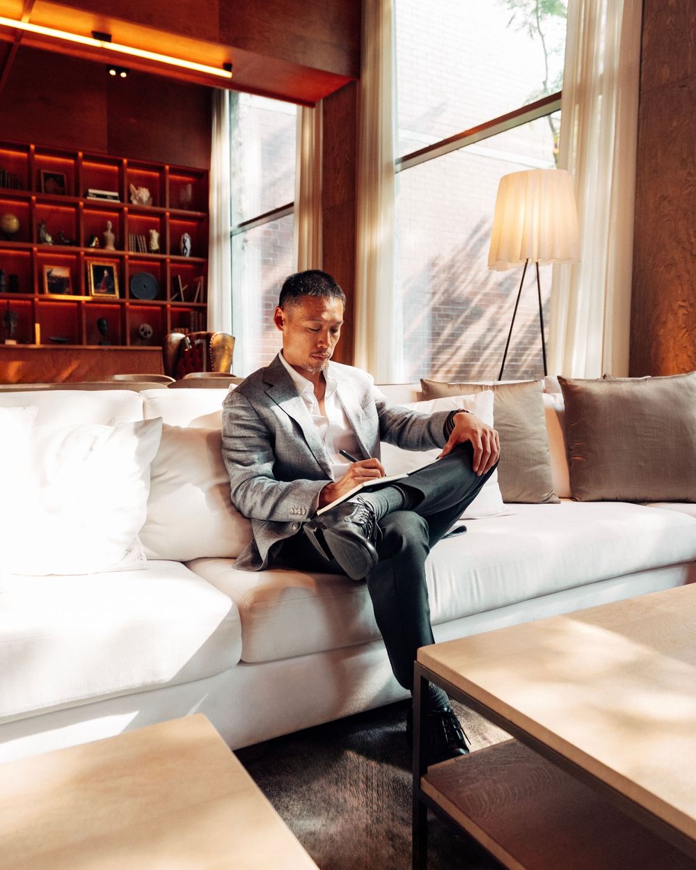 Professional in a gray suit sits thoughtfully on white couch in modern office space with natural lighting.