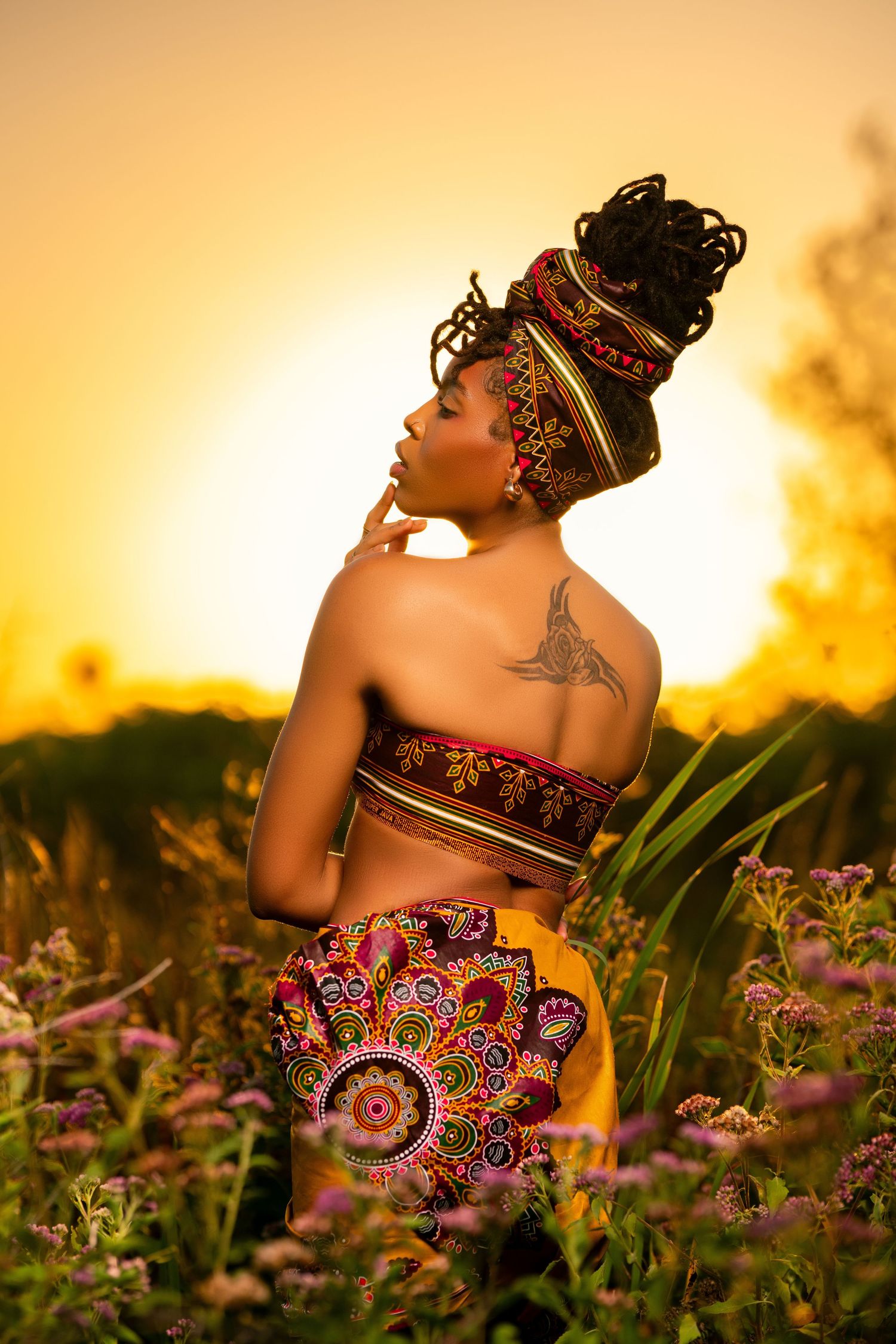 A silhouetted figure in a floral dress poses gracefully among wildflowers during a golden sunset.