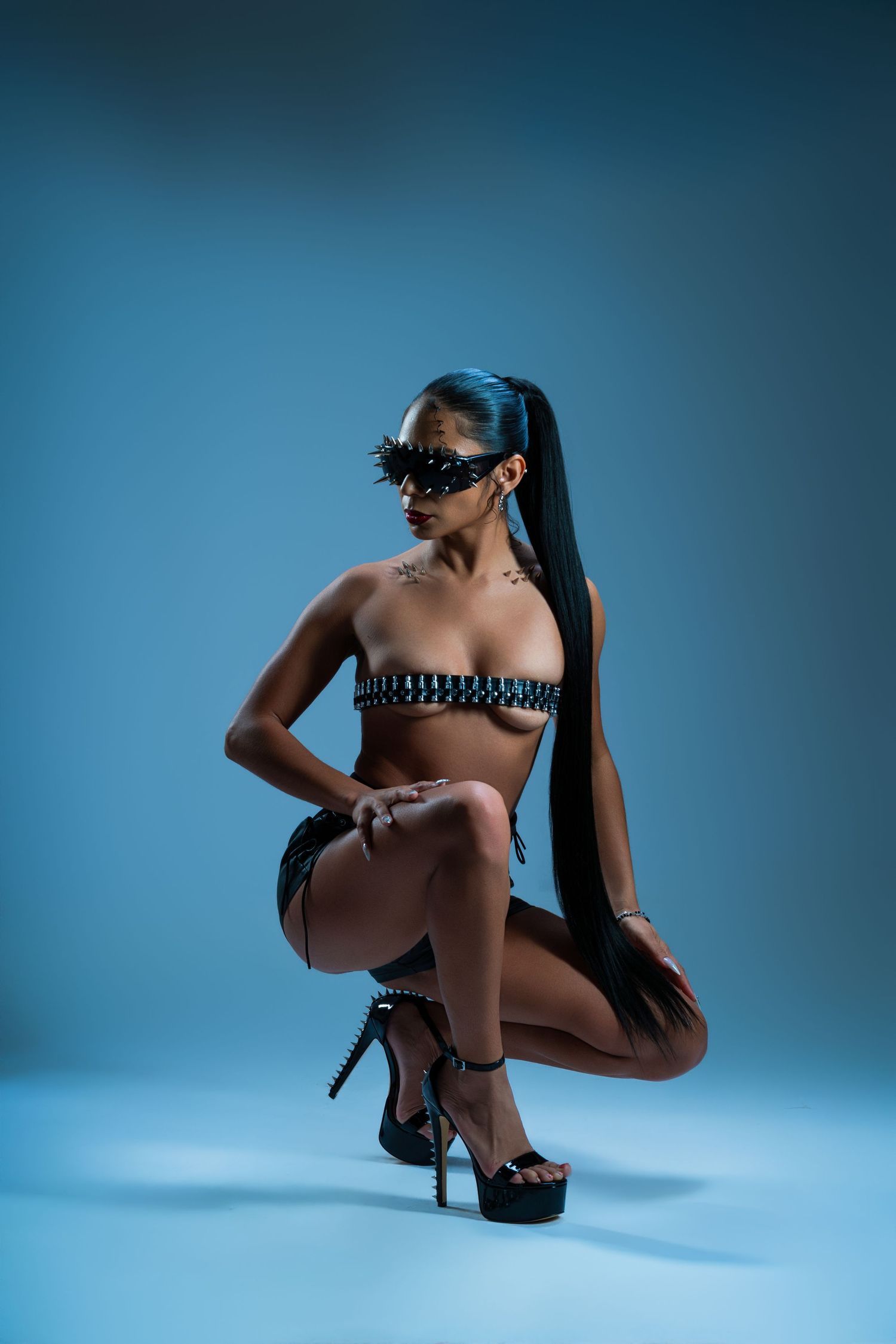 Artistic nude silhouette poses against blue background wearing high heels in minimalist studio setting.