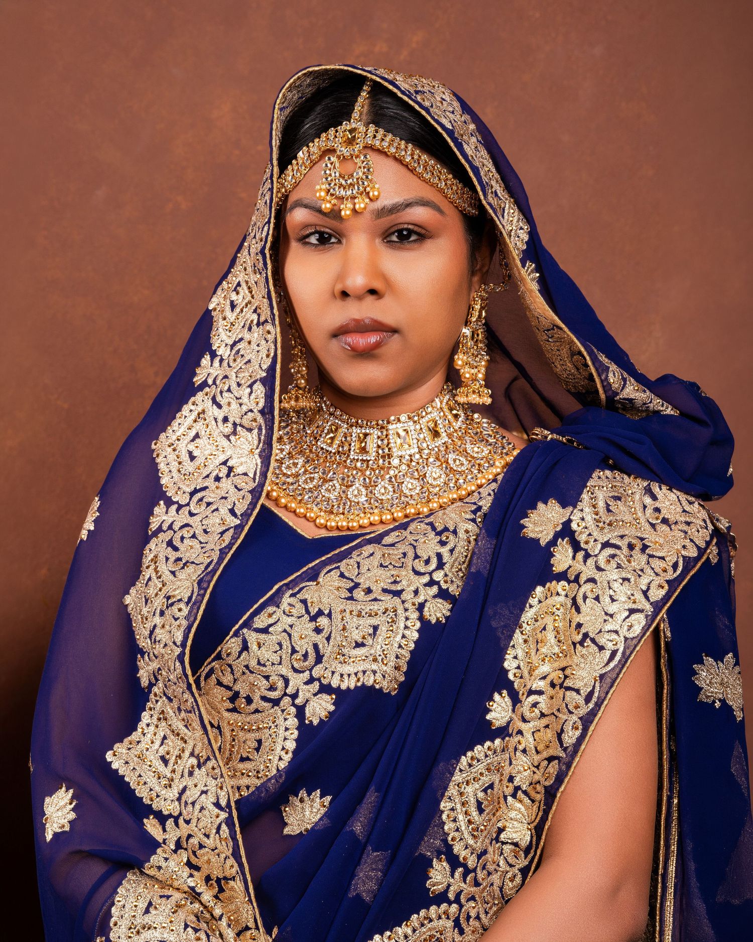 Traditional Indian bridal portraits in royal blue and gold embroidered sari with ornate jewelry and makeup.