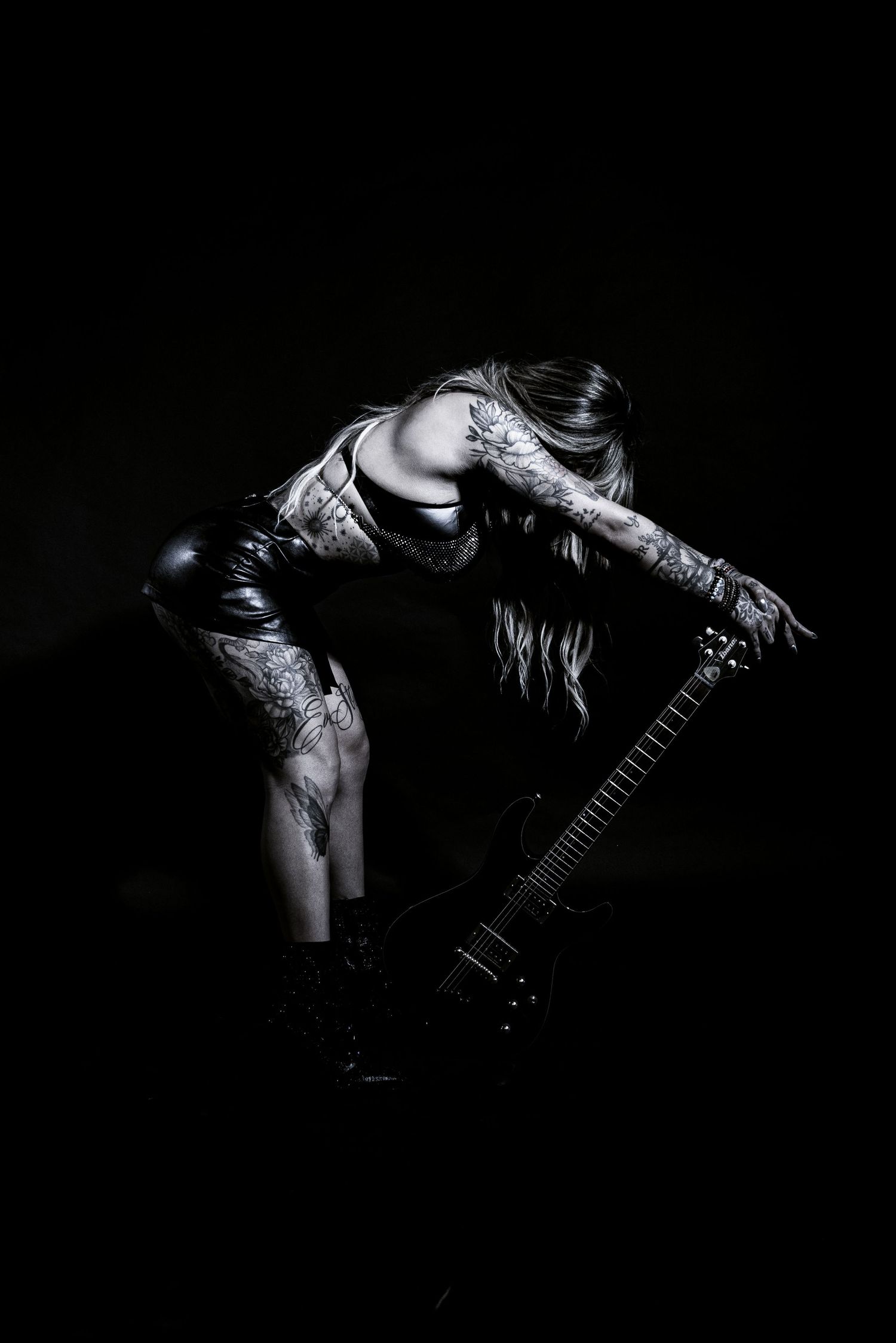 Dramatic black and white photo of tattooed musician with guitar in dynamic pose.