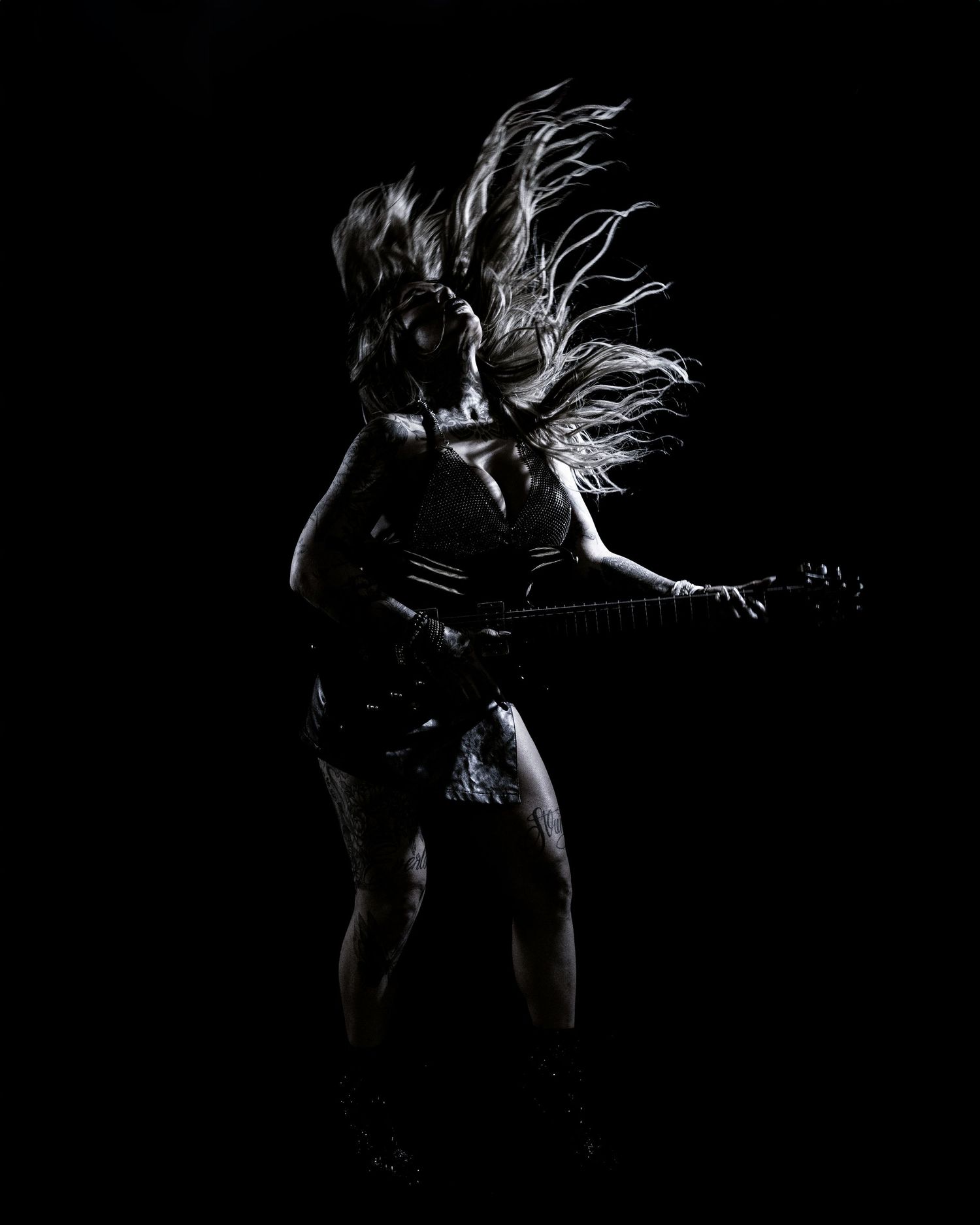 Dramatic silhouette of guitarist with flowing hair performing against dark background.