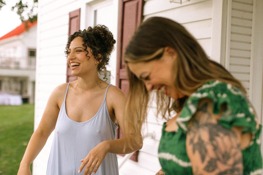 Two people sharing a candid laughing moment outdoors on a sunny day.