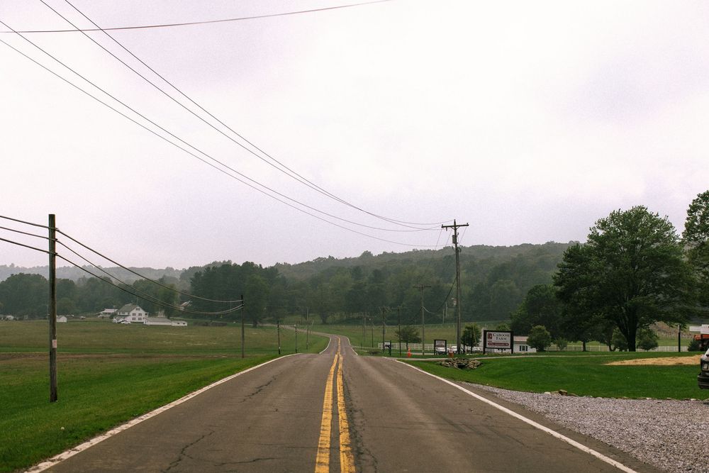 Rural country road stretching into the distance with power lines and green fields on both sides.